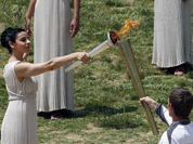 An actress as high priestess, passes on the Olympic flame to Spyros Gianniotis, a 32-year-old Liverpool-born swimmer, who won a silver medal for Greece in the 5-kilometer open water event four years ago in Beijing, during the lighting of the flame ceremony in Greece.