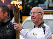 Bobby Charlton carrying the Olympic Flame on the Torch Relay leg between Salford and Moss Side in Manchester, England.