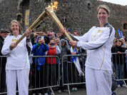 Kathleen Irvine, left, passes Lisa Hickson the Olympic Flame outside of Carrickfergus Castle in Carrickfergus Northern Ireland during the Olympic Torch Relay.