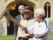 This image made available by LOCOG shows Queen Elizabeth II, second right, and the Duke of Edinburgh watching the Torch Kiss as Torchbearer 073 Gina Macgregor, right, passes the Olympic Flame to Torchbearer 074 Phillip Wells, left, outside Windsor Castle, Windsor, England.