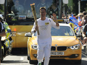 In this photo provided by LOCOG, torchbearer and former cricket captain Michael Vaughan carries the Olympic Flame on the Torch Relay leg through Hillingdon, England.